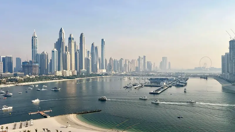 The Dubai coastline and marina towers on a bright day, with boats in the bay