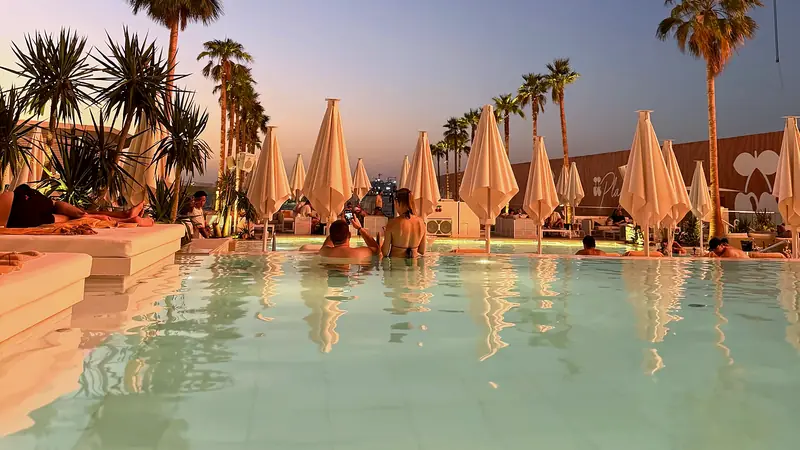 A hotel pool in Dubai at dusk with palm trees and parasols