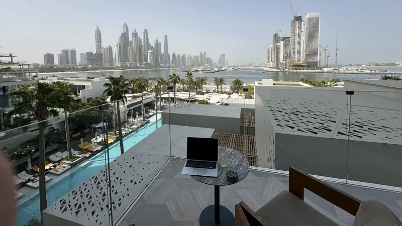 A laptop on a table on a terrace above a pool, with the Dubai Marina skyline behind